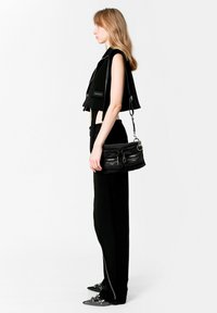 Top corto negro con mangas de capucha, combinado con pantalones negros de talle alto y un pequeño bolso negro de hombro. Detalles de herrajes plateados visibles.