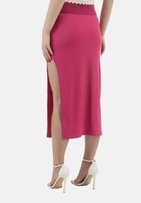 Gonna midi fucsia a costine con uno spacco laterale, caratterizzata da un punto vita aderente e una texture morbida. Abbinata a scarpe con tacco alto e cinturino alla caviglia bianche.