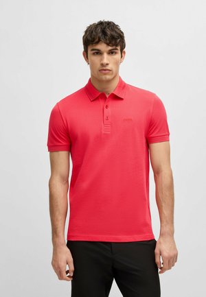 Polo shirt rossa realizzata in tessuto liscio, con colletto classico, tre bottoni e un logo discreto sul lato sinistro del petto. Maniche corte.