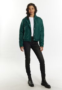 Giacca a vento verde con zip e chiusura a scatto, polsini e orlo elastici; abbinata a pantaloni neri slim e stivali neri chunky.