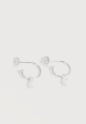 Μικρά ασημένια σκουλαρίκια κρίκοι με κρεμαστά ασημένια σταυρουδάκια και κλεισίματα push-back σε λευκό φόντο.