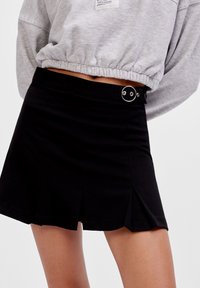 Gonna mini nera plissettata con una superficie liscia e una fibbia circolare argentata. Abbinata a un crop sweatshirt grigio sopra.