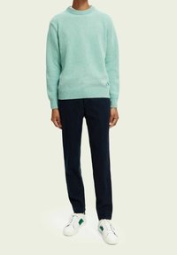 Maglione in maglia color teal chiaro con collo rotondo e polsini a coste, abbinato a pantaloni blu scuro e sneakers bianche con dettagli verdi.