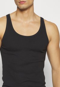 Débardeur noir en coton lisse. Présente une coupe ajustée avec de larges bretelles et un col rond.