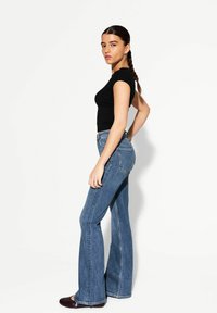 Schwarzes, figurbetontes T-Shirt kombiniert mit hellblauen, weit geschnittenen Jeans mit hoher Taille und auffälligen Nähten, ergänzt durch dunkelglänzende Schuhe.