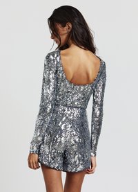 Tutina argento con paillettes, maniche lunghe, scollatura profonda sulla schiena e pantaloncini. Superficie testurizzata con linee orizzontali di paillettes.