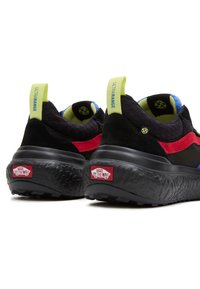 Černé a červené tenisky s texturovaným svrškem, silnou černou podrážkou a barevnými akcenty v neonově zelené a modré; mají také značkové patní vložky.