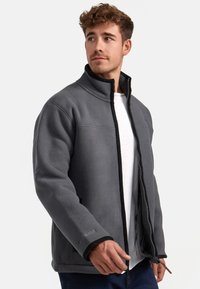 Chaqueta de forro polar gris con un collar alto, acentos negros y cierre con cremallera. Cuenta con mangas largas y bolsillos laterales.