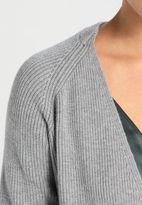 Grauer gerippter Cardigan mit V-Ausschnitt, mit einem strukturierten Strickmuster und Raglanärmeln. Weicher Stoff verbindet Komfort und Wärme.