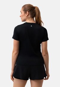 Black athletic t-shirt with short sleeves, smooth texture, and a small logo on the back. Paired with black shorts, showcasing a fitted design.