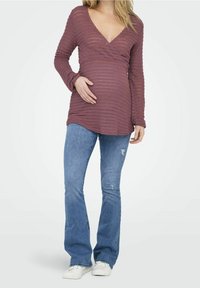 Haut de maternité en tissu côtelé bordeaux avec un col en V et des manches longues, associé à un jean flare bleu délavé et des baskets blanches.