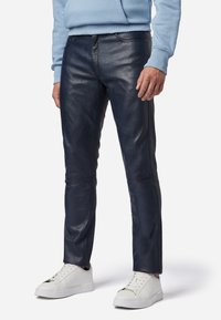 Marine leren broek met een slim fit, met een zachte textuur en subtiele stiksels. Gecombineerd met witte sneakers voor contrast.
