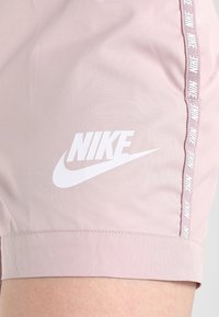 Helle, pink Nike-Shorts mit glatter Textur, die ein auffälliges weißes Logo auf der Vorderseite und einen gebrandeten weißen Streifen an den Seiten aufweisen.