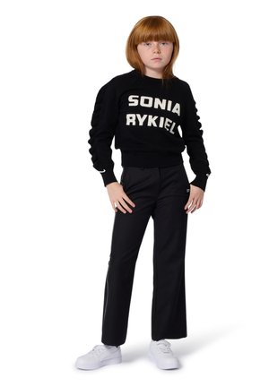 Zwarte gebreide trui met witte "SONIA RYKIEL" tekst, geribde kraag. Zwarte broek met zijritsen, gecombineerd met witte sneakers.
