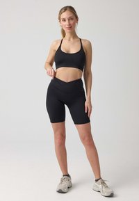 Zwart sportief crop-top met dunne bandjes, gecombineerd met hoge zwarte fietsbroek. De stof is glad met een subtiele glans.
