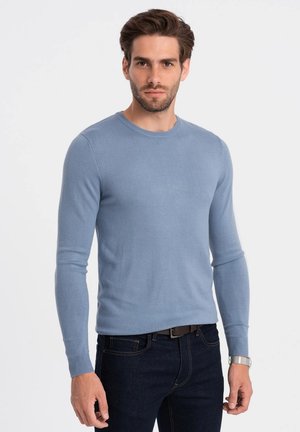 Un pull en maille bleu clair avec un col rond et des manches longues, fabriqué à partir d'un matériau lisse, associé à un jean en denim foncé.
