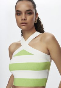 Top corto a righe verde e bianche con design a incrocio sulla schiena. Realizzato in tessuto a coste, presenta una silhouette aderente e una texture liscia.
