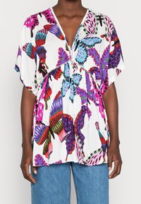 Short-sleeve, V-neck blouse in white with a butterfly pattern in red, pink, blue, and purple. Features gathered waist and decorative stitching.