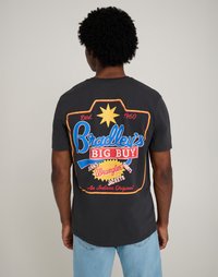 Fekete pamut póló színes grafikai nyomattal a hátulján, amely szöveget és csillagmotívumot ábrázol, rövid ujjú és laza szabású.