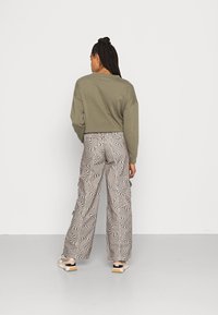 Sweatshirt corta em verde-oliva combinado com calças largas de cintura alta, apresentando um padrão ondulado em preto e branco, usadas com ténis em tons neutros.
