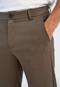 Bruine, gestructureerde broek met een voorste knoop, zijzakken en een rechte pasvorm. De stof heeft een gladde, op maat gemaakte uitstraling.