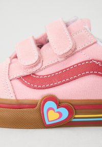 Baskets en toile rose avec des détails en cuir rouge, bandes Velcro et un design de cœur multicolore sur le côté. Semelle en caoutchouc avec des accents rayés.
