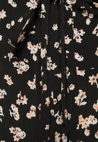 Svart blommig blus med små vita och persikofärgade blommor, lättviktig tyg och en knytdetalj vid halsen. Har en slät och mjuk yta.