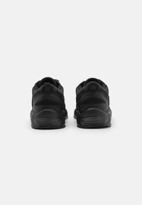 Black athletic shoes with a cushioned sole, textured fabric upper, and reinforced heel, featuring a looped pull tab at the back.