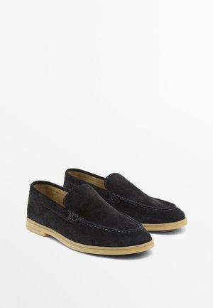 Par sort rågummisko i sort ruskind med beige gummisåler, runde tæer og synlige syningsdetaljer.