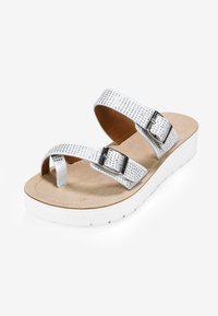 Sandalia de planta plana sintética plateada con dos cintas ajustables, adornada con acentos de rhinestone y una plantilla acolchada en color beige sobre una suela blanca.