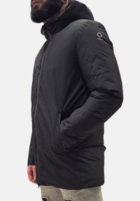 Giacca nera isolata con chiusura a zip, cappuccio regolabile e tasche laterali. La texture liscia e il design aderente migliorano il calore e il comfort.