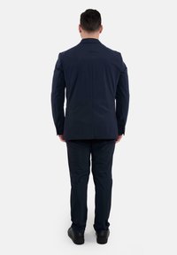 Abito blu navy, con giacca strutturata e pantaloni su misura, realizzato in tessuto liscio. La vista dal retro mostra linee pulite e dettagli minimi.