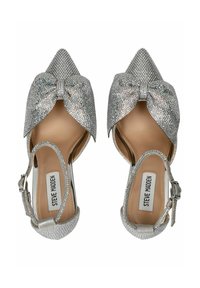 Zapatos de tacón alto plateados con punta en forma de almendra, adornados con un lazo y strass. Cuentan con una correa y un forro interior suave.