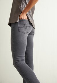 Jeans gris ajustados hechos de mezclilla, con un bolsillo trasero que presenta un diseño de costura curvada y una textura suave.