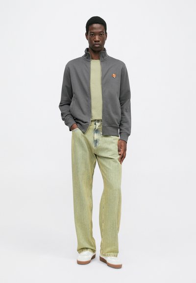 Gray zip-up jacket with high collar, light green t-shirt underneath, and loose light green striped jeans. White sneakers and subtle logo detail.