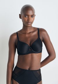 Zwarte draadloze bh met gladde cups, verstelbare banden en kantafwerking. Gecombineerd met zwarte hoge taille briefs met geperforeerde meshpanelen.