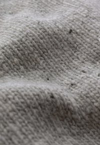 Šedá tkanina s tkaným vzorem, která vykazuje texturovaný povrch s viditelnými vlákny a jemnými odstínovými variacemi, což vytváří měkký a přívětivý vzhled.