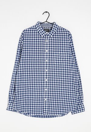 Chemise à manches longues à carreaux bleus et blancs, col boutonné, poche poitrine, suspendue sur un cintre noir sur fond blanc.