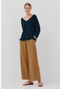 Navy V-Ausschnitt-Pullover kombiniert mit beigen weit geschnittenen Hosen. Der Pullover hat eine lockere Passform, die Hosen haben eine strukturierte Oberfläche. Schlichte Sandalen.
