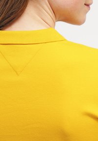 Gul polo skjorta med ribbad krage, som har ett texturerat tyg och en V-formad detalj vid bakhalsen.