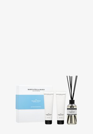 Set di articoli essenziali per il bagno in una scatola bianca con una fascia blu. Contiene due tubetti bianchi etichettati body wash e un altro prodotto, oltre a un diffusore.