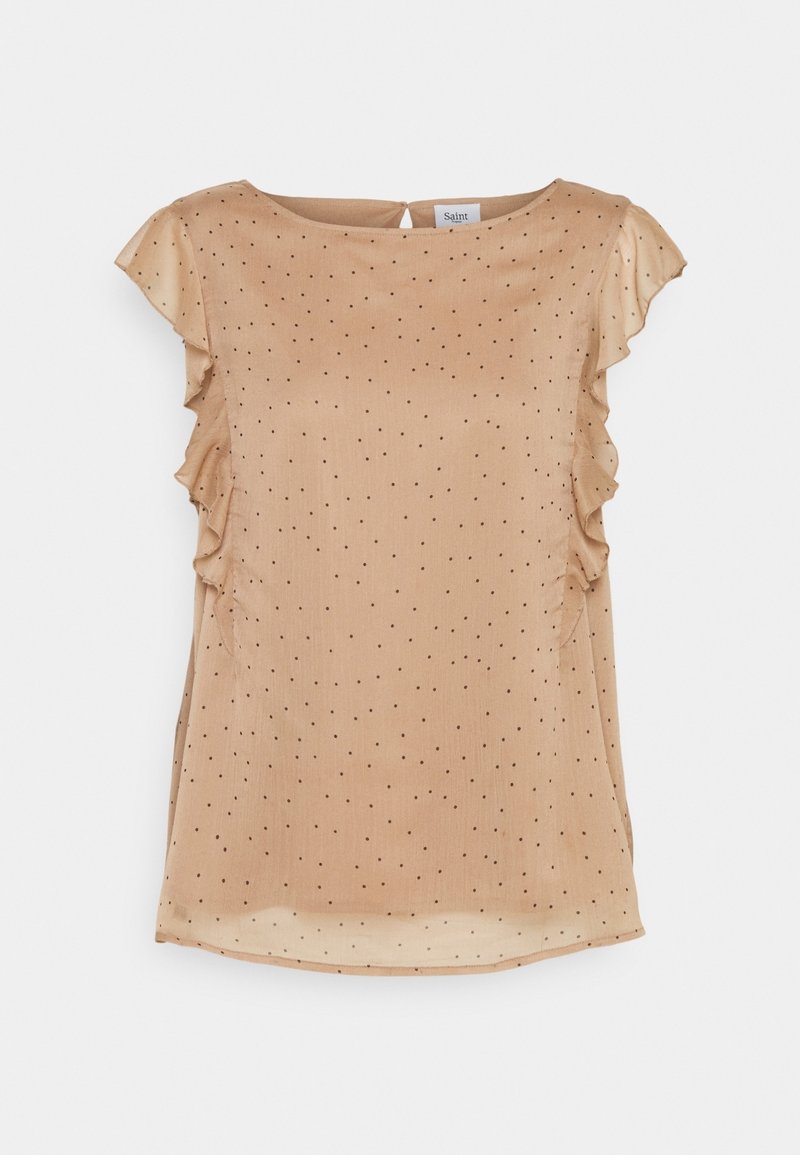 Blouse en satin beige à pois noirs, avec des accents à volants sur les épaules, un décolleté en arrondi et un ourlet légèrement incurvé. Texture lisse sur toute la surface.