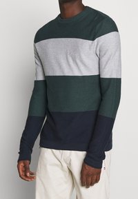 Pull rayé vert foncé, gris clair et bleu marine avec un col rond et des manches longues, fabriqué dans un tissu tricoté texturé.
