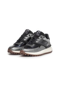 Un paio di sneakers basse nere e argento con lacci neri, suole texturizzate e patch con logo sulla linguetta, posizionate in avanti su sfondo bianco.