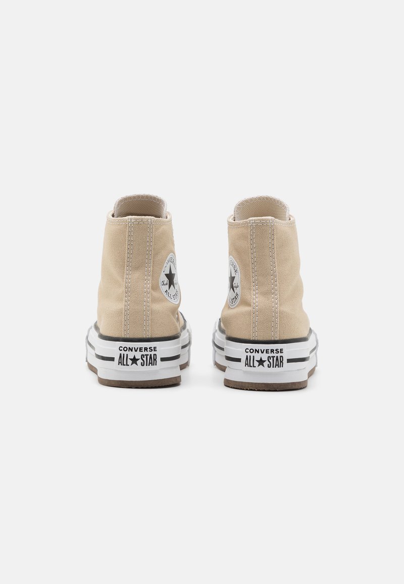 Zapatillas altas de lona beige con un logo de estrella negra redonda, detalles blancos y suelas de goma negra con franjas características.