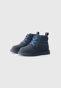 Stivali alla caviglia in suede blu navy con lacci azzurri, punta tonda e suole in gomma. Presentano dettagli di cucitura e linguette per una facile calzata.