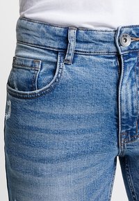 Vaqueros de denim de un azul claro con un diseño de cinco bolsillos, costuras visibles y una textura desgastada en la zona del muslo.