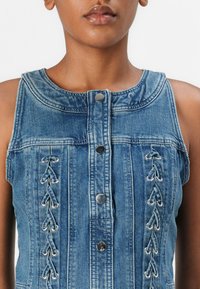 Robe sans manches en denim bleu clair avec un col rond, des boutons sur le devant et des accents en dentelle avec des œillets sur les côtés.