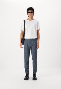 Weißes T-Shirt, taillierte blaue karierte Hose, schwarze Sonnenbrille und schwarze Tasche. Die Schuhe sind schwarz mit einer glatten Oberfläche. Einfaches, minimalistisches Design.