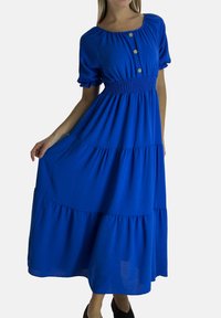 Blauwe katoenen maxi-jurk met pofmouwen, een geplooide taille en knoopdetails. Heeft een gelaagde rok en een vloeiend ontwerp.